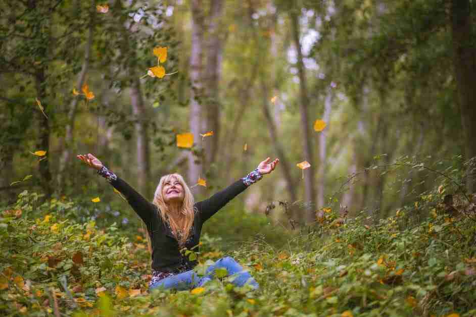 a woman sitting in the grass with her arms up and the air falling from the ground