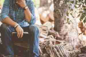 Man sitting besides a tree appearing to be mediating or praying with a Bible in his hands