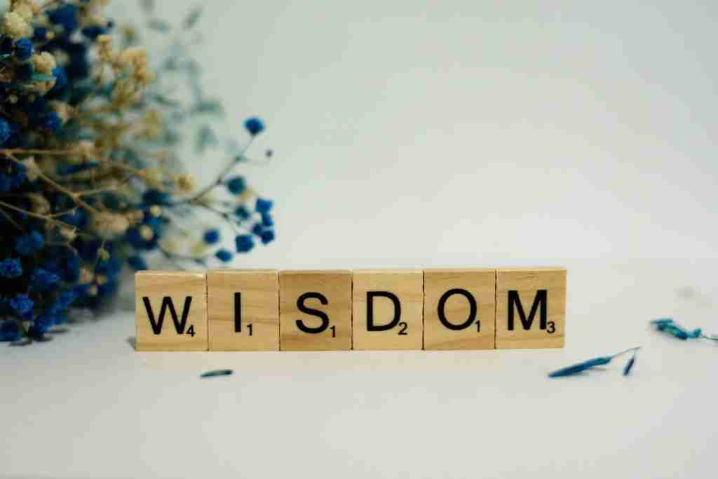 a wooden block spelling the word wisdom next to a bouquet of flowers