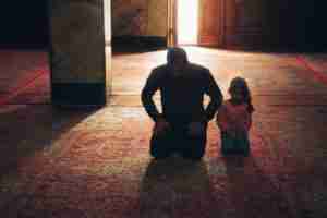 Man and Child Kneeling with head bowed in what appears to be prayer on carpet within a building