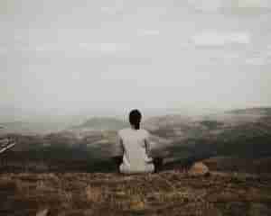 woman sitting on cliff overlooking mountains during daytime