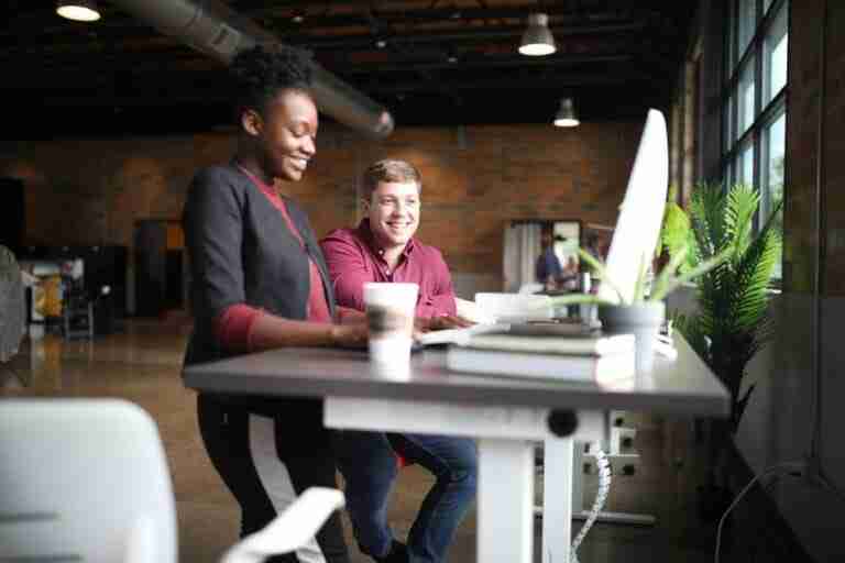 Two people working together at a desk witha computer and each are smiling