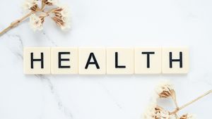 Creative arrangement of scrabble tiles spelling 'Health' with white flowers on a marble surface.